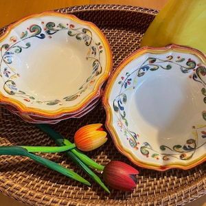 May include: Two white ceramic bowls with scalloped edges and colorful floral designs, stacked on a woven tray. The bowls have a yellow and orange border. Decorative wooden tulips are also on the tray.