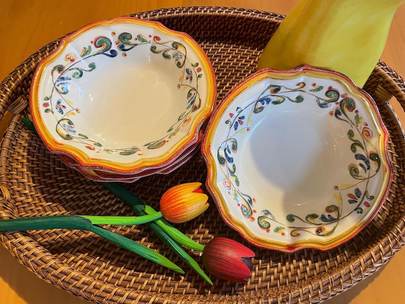 May include: Two white ceramic bowls with scalloped edges and colorful floral designs, stacked on a woven tray. The bowls have a yellow and orange border. Decorative wooden tulips are also on the tray.