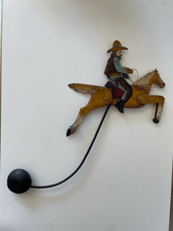 An authentic painted metal folk art cowboy-on-horse pendulum sculpture — the kind of thing you find once at an estate sale and never again.