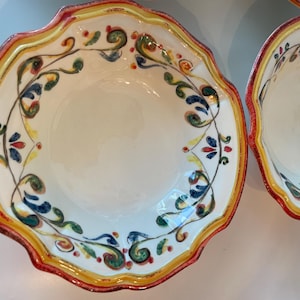 May include: White ceramic bowls with scalloped edges and colorful floral designs. The rims are trimmed with red, yellow, and orange paint. The bowls have a decorative pattern of green, blue, and red leaves and flowers.