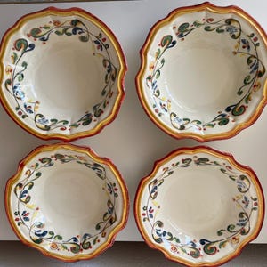 May include: Four ceramic bowls with scalloped edges. The bowls have a cream-colored interior and are decorated with a floral vine pattern in green, blue, and yellow. The rims are trimmed with a red and yellow border.