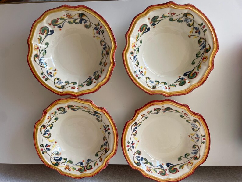 May include: Four ceramic bowls with scalloped edges. The bowls have a cream-colored interior and are decorated with a floral vine pattern in green, blue, and yellow. The rims are trimmed with a red and yellow border.