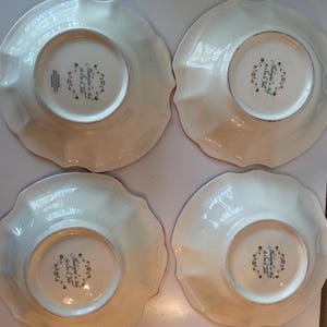 May include: Four off-white, scalloped-edge plates. The underside of each plate features a central design with text that reads "Made in Italy for Sur La Table". The plates have a glossy finish.