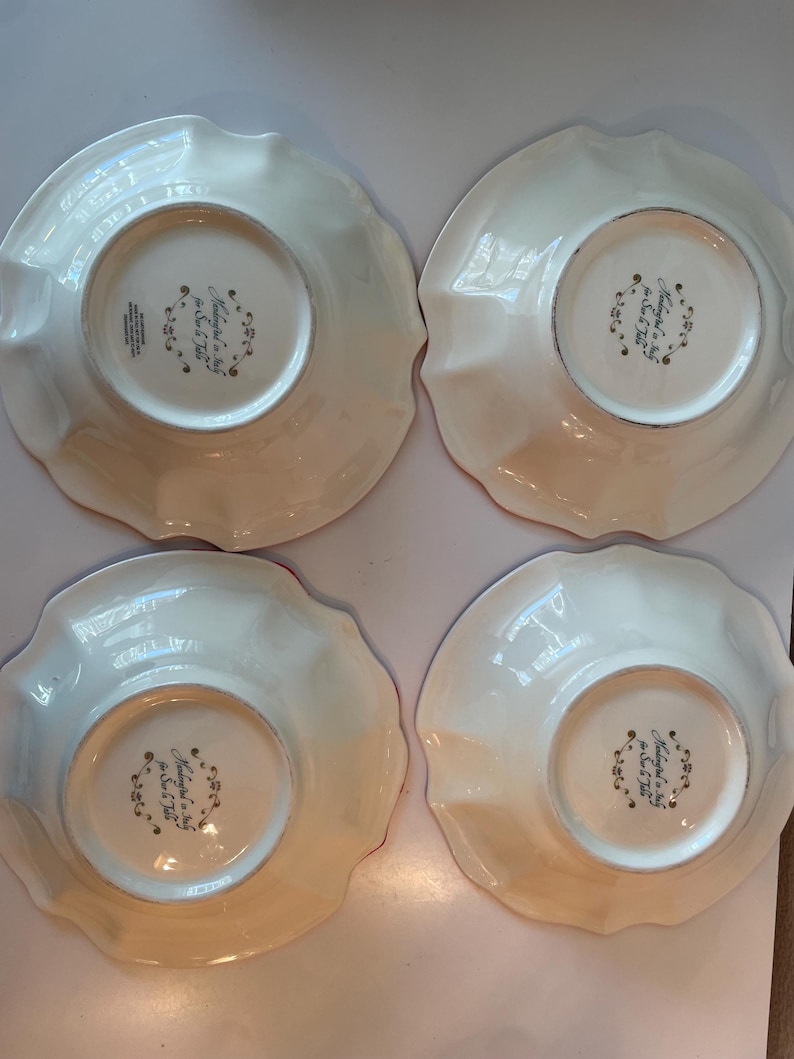 May include: Four off-white, scalloped-edge plates. The underside of each plate features a central design with text that reads "Made in Italy for Sur La Table". The plates have a glossy finish.