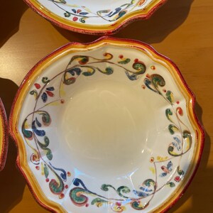 May include: A set of white ceramic bowls with a scalloped edge. The rims are decorated with a red and yellow border, and the interior features a colorful floral design in green, blue, and yellow.