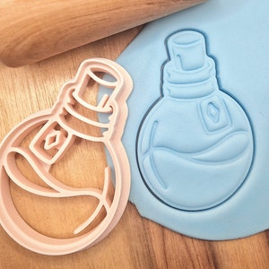 Op de afbeelding: Twee koekjesvormen in de vorm van een fles met een stop. De vorm links is roze en de vorm rechts is blauw.