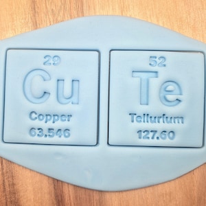 Peut inclure: Un moule en silicone bleu avec deux carrés. Chaque carré a un contour blanc et contient un symbole d'élément chimique et des informations. Le premier carré indique "29 Cu Cuivre 63,546". Le deuxième carré indique "52 Te Tellure 127,60".