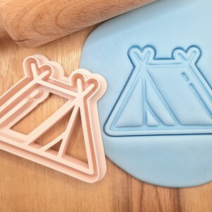 May include: Two plastic cookie cutters in the shape of a tent. One cutter is light pink and the other is light blue.