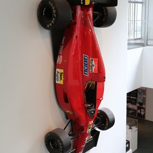 Puede incluir: Un coche de carreras de Fórmula 1 rojo montado en una pared blanca. El coche tiene las palabras "Marlboro", "FIAT" y "Agip" en el lateral. El coche está boca abajo, con las ruedas mirando hacia el techo.