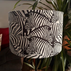 May include: Black and white zebra print lampshade. The lampshade is cylindrical and features a repeating pattern of zebras.