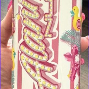 Puede incluir: Un vaso con tem&aacute;tica de algod&oacute;n de az&uacute;car con un fondo a rayas rosas y blancas. El vaso presenta las palabras "Cotton Candy" y "Energy" en una fuente l&uacute;dica, junto con un dise&ntilde;o "Zzz" y elementos decorativos.