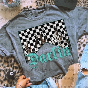 May include: A gray long-sleeve shirt featuring a graphic with a black and white checkered pattern, flames, and the word "Darlin" in turquoise script. The shirt is a casual style.
