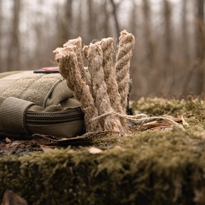 Könnte beinhalten: Nahaufnahme eines Bündels natürlicher Jute-Schnur, ein gängiges Material zum Feuermachen, das auf einer moosigen Oberfläche in einer Waldumgebung liegt.