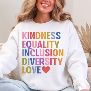 May include: White sweatshirt with the words "KINDNESS EQUALITY INCLUSION DIVERSITY LOVE" in rainbow colors. A red heart is below the word "LOVE". The sweatshirt is a crew neck style.