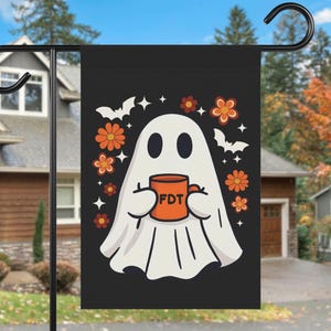 May include: A black garden flag featuring a white ghost holding an orange mug with the letters FDT printed on it. The design includes orange and red flowers, white bats, and small star shapes surrounding the ghost on a dark background.
