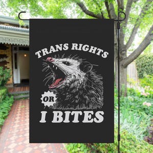 May include: Black garden flag with a white opossum illustration and the text "Trans Rights or I Bites".
