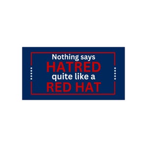 May include: A blue and white sign with the text "Nothing says HATRED quite like a RED HAT" in red and white letters.