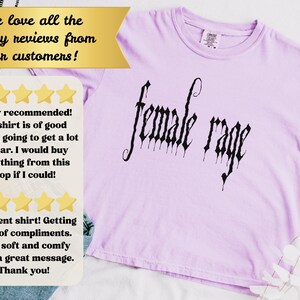 May include: A light purple t-shirt with the words "female rage" in a gothic font. The shirt has a crew neck and short sleeves. The image also includes customer reviews.
