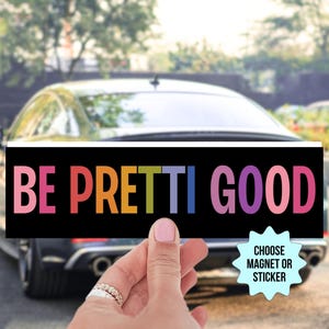 May include: A black rectangular magnet or sticker with the words "BE PRETTI GOOD" in rainbow-colored letters. The words are displayed against a black background. The image also includes a car and the text "CHOOSE MAGNET OR STICKER".