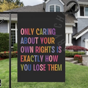 May include: A black garden flag with the text "ONLY CARING ABOUT YOUR OWN RIGHTS IS EXACTLY HOW YOU LOSE THEM" in rainbow colors.