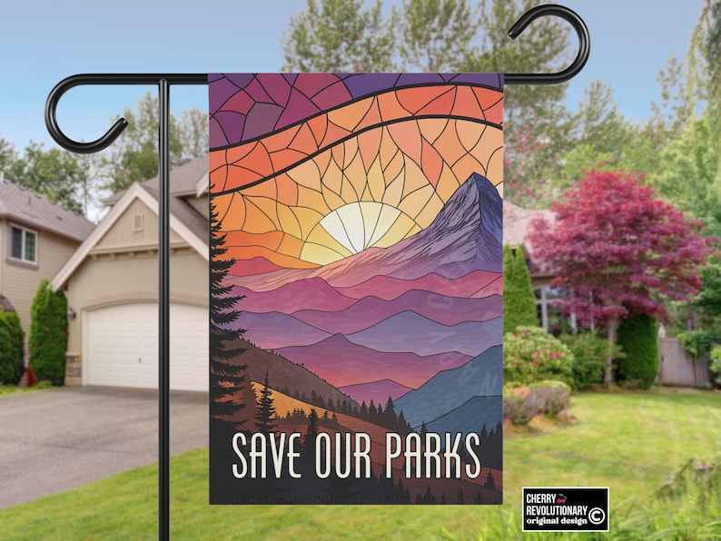 Puede incluir: Una bandera de jard&iacute;n con un dise&ntilde;o de paisaje monta&ntilde;oso y una puesta de sol en tonos naranja, amarillo y morado. El texto "SAVE OUR PARKS" se muestra en blanco. La bandera est&aacute; colgada de un poste de metal negro.