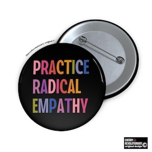 May include: A black button with the words "PRACTICE RADICAL EMPATHY" in rainbow colors. The button is round with a metal pin back. The button is a CherryRevolutionary original design.