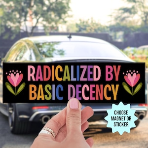 May include: Black rectangular magnet or sticker with the text "RADICALIZED BY BASIC DECENCY" in colorful letters. The design includes floral elements on each side. The background shows a car.