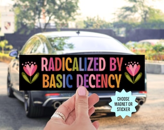 May include: Black rectangular magnet or sticker with the text "RADICALIZED BY BASIC DECENCY" in colorful letters. The design includes floral elements on each side. The background shows a car.