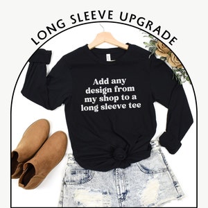 May include: Black long-sleeve t-shirt with the text "Add any design from my shop to a long sleeve tee" in white lettering. The shirt is displayed on a hanger with a pair of brown ankle boots and denim shorts.