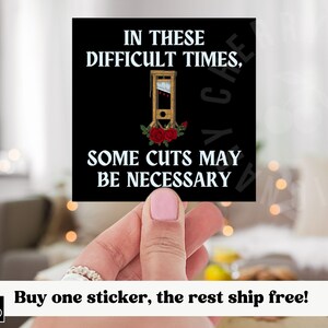 May include: A black square sticker with white text that reads "In these difficult times, some cuts may be necessary."  A small image of a guillotine with red roses is in the centre of the sticker.