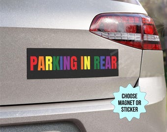 May include: A black rectangular magnet with the text "PARKING IN REAR" in rainbow colors is affixed to the back of a silver car. The magnet is a car accessory. A light blue starburst graphic says "CHOOSE MAGNET OR STICKER".