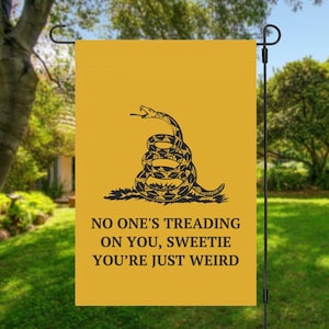 Puede incluir: Una bandera de jardín amarilla con un diseño de serpiente negra y el texto "No one's treading on you, sweetie you're just weird".