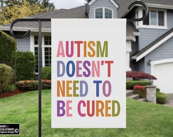 Peut inclure: Un drapeau de jardin blanc avec le texte "AUTISM DOESN'T NEED TO BE CURED" en lettres majuscules colorées. Le drapeau est affiché sur un support en métal noir dans un jardin résidentiel.