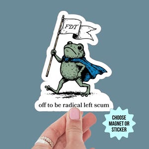 Puede incluir: Una pegatina con una rana de dibujos animados con una capa azul, sosteniendo una bandera con "FDT". La rana camina, con las palabras "off to be radical left scum" debajo. Una estrella dice "CHOOSE MAGNET OR STICKER."
