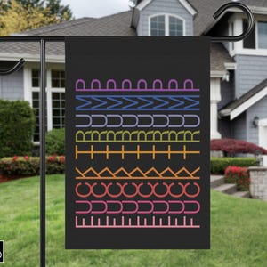 May include: Black garden flag with a colorful geometric pattern. The design features rows of various shapes and lines in shades of purple, blue, green, orange, and pink. The flag is displayed on a black metal stand in a residential yard.