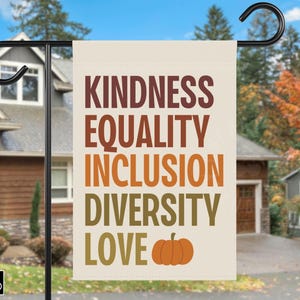 Può includere: Una bandiera da giardino rettangolare con le parole "KINDNESS, EQUALITY, INCLUSION, DIVERSITY, LOVE" in lettere marroni, arancioni e verdi, con una grafica di zucca arancione. La bandiera è su un supporto di metallo nero davanti a una casa.