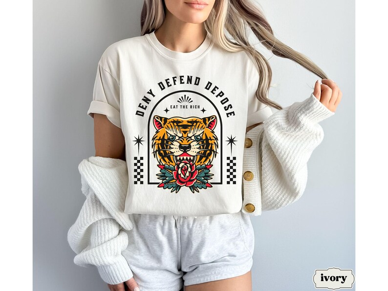 May include: White t-shirt with a tiger graphic and the text "Deny Defend Depose Eat the Rich".