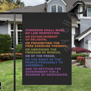 May include: Black garden flag with the text of the First Amendment of the U.S. Constitution in a rainbow gradient. The flag is displayed outdoors in front of a house with a black metal pole.