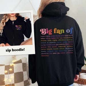 May include: Black zip-up hoodie with the text "Big fan of human rights" on the front and a list of human rights on the back. The text is in a rainbow color scheme. The hoodie is displayed in a polaroid-style frame.