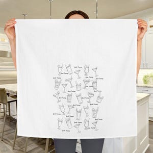 Peut inclure: Une serviette de cuisine blanche avec une illustration en noir et blanc de diff&eacute;rents verres &agrave; cocktail. Les verres sont dispos&eacute;s en forme de c&oelig;ur et chaque verre porte le texte "Drink Champs" &eacute;crit en dessous.