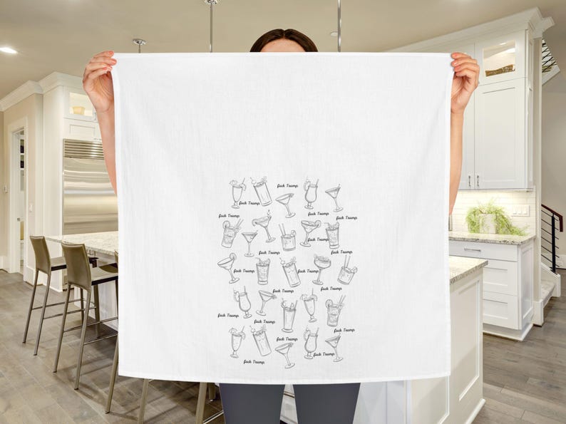 Peut inclure: Une serviette de cuisine blanche avec une illustration en noir et blanc de diff&eacute;rents verres &agrave; cocktail. Les verres sont dispos&eacute;s en forme de c&oelig;ur et chaque verre porte le texte "Drink Champs" &eacute;crit en dessous.