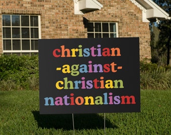 May include: A black sign with the words "christian -against- christian nationalism" in rainbow colors.