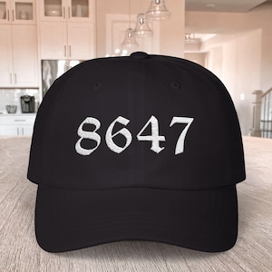 May include: A black baseball cap with the number "8647" embroidered in white. The hat is made of a durable fabric and has a curved brim. The numbers are in a bold, stylized font.