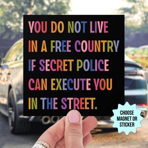 May include: Black square magnet or sticker with the text "YOU DO NOT LIVE IN A FREE COUNTRY IF SECRET POLICE CAN EXECUTE YOU IN THE STREET." The text is in various colors. A small starburst graphic says "CHOOSE MAGNET OR STICKER."