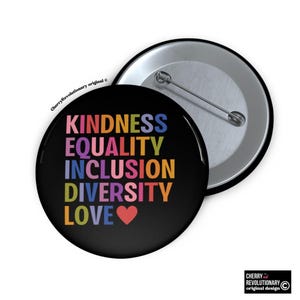 May include: A black button badge with the words "KINDNESS, EQUALITY, INCLUSION, DIVERSITY, LOVE" in rainbow colours. A red heart symbol is below the word "LOVE". The badge is next to a silver-coloured pin back.