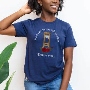 Puede incluir: Una camiseta azul marino con un gr&aacute;fico blanco de una guillotina con el texto "Faire les coupes n&eacute;cessaires - Depuis 1789 -"