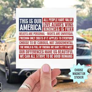 May include: A white square magnet or sticker with the text "THIS IS OUR AMERICA" in blue and red, along with inspirational phrases. The image is held in front of a car.