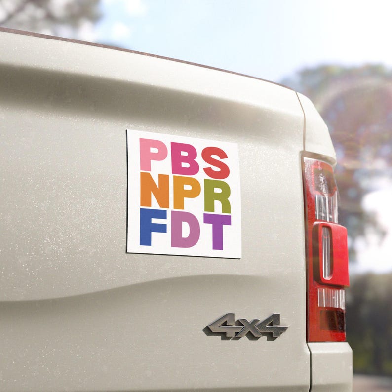 May include: A white rectangular magnet with the text "PBS NPR FDT" in colorful block letters. The magnet is affixed to the back of a white vehicle.
