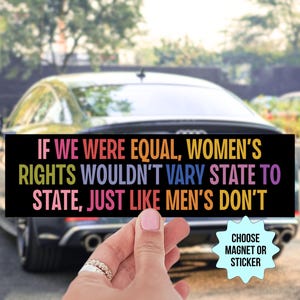 May include: A rectangular black bumper sticker featuring multi-colored text that reads: IF WE WERE EQUAL, WOMEN'S RIGHTS WOULDN'T VARY STATE TO STATE, JUST LIKE MEN'S DON'T. A light blue starburst graphic in the corner displays the text CHOOSE MAGNET OR STICKER.