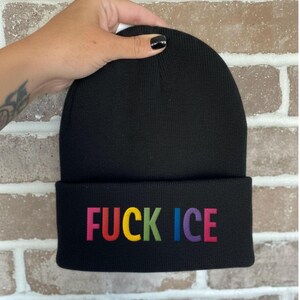 May include: A black beanie with the embroidered text "FUCK ICE" in rainbow colors. The beanie is made of a soft, knitted material and has a folded brim.